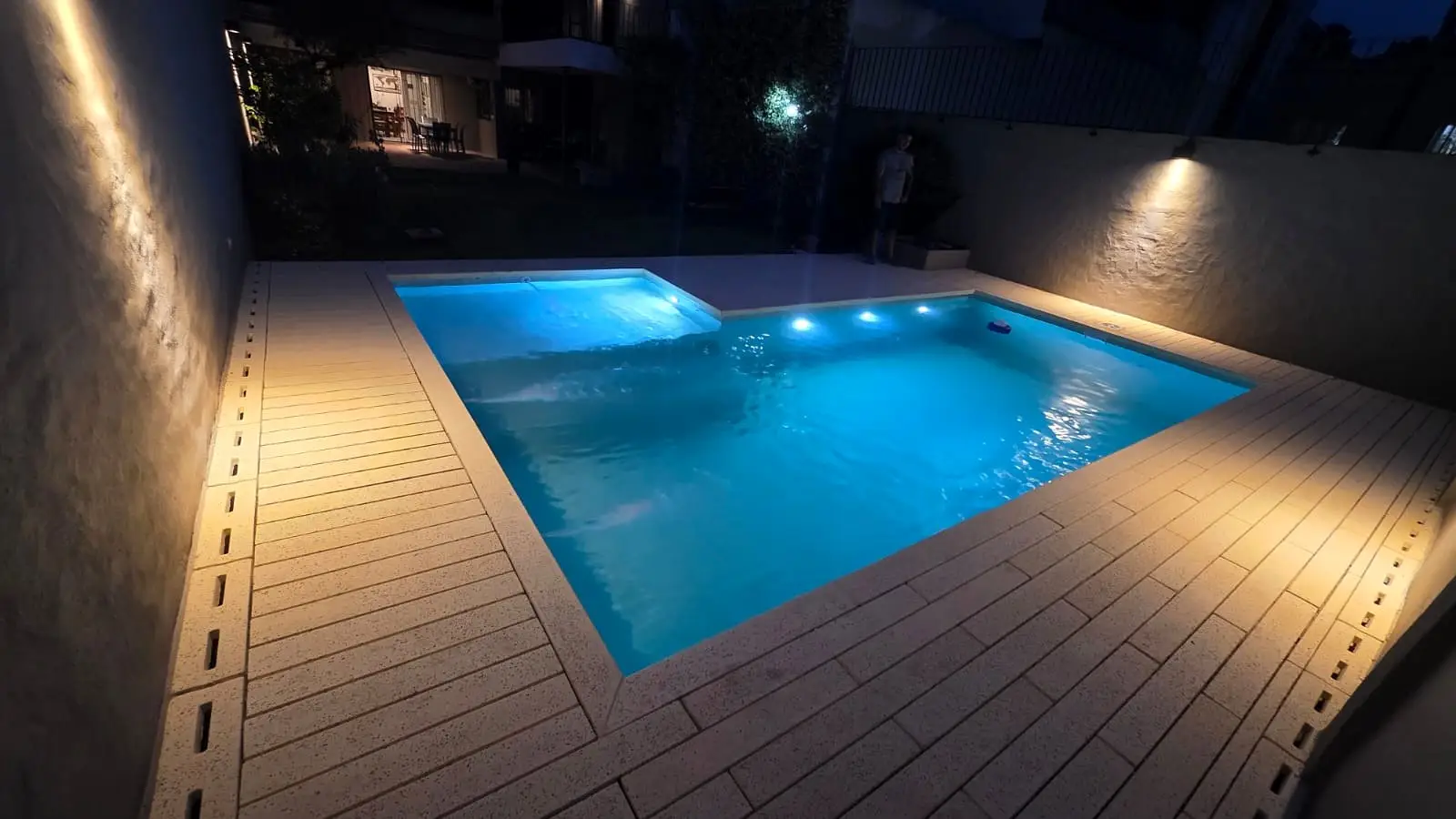 Piscina de hormigón en Belgrano iluminada de noche, rodeada por un solárium atérmico color arena