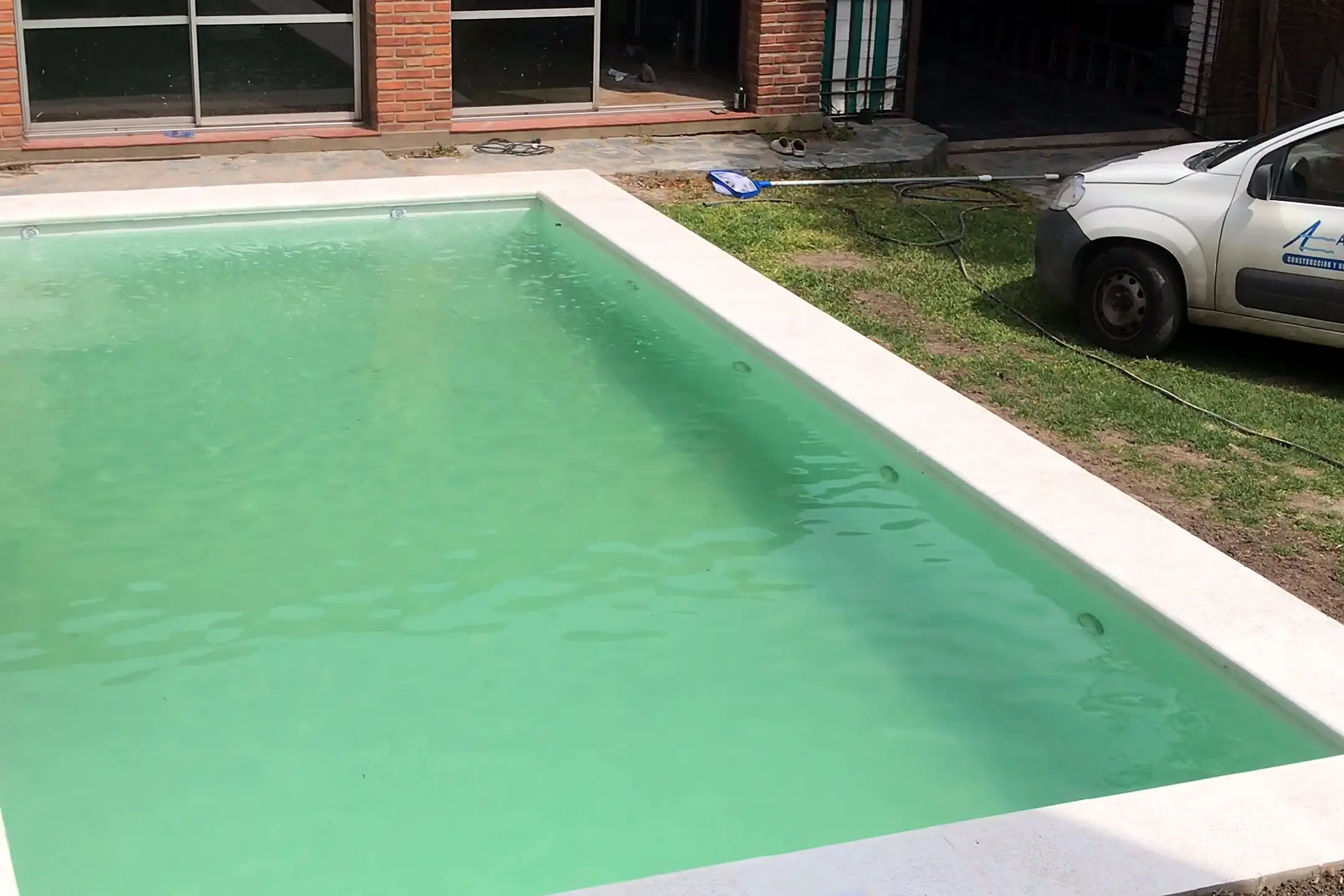 Piscina de hormigón terminada frente a una casa de ladrillo, con borde atérmico blanco