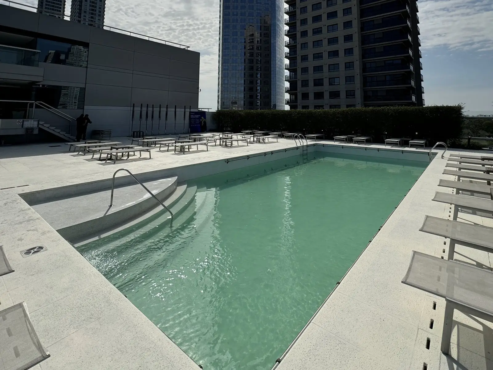 Piscina exterior del hotel Hilton en Puerto Madero renovada y llena, con reposeras y las torres del barrio de fondo