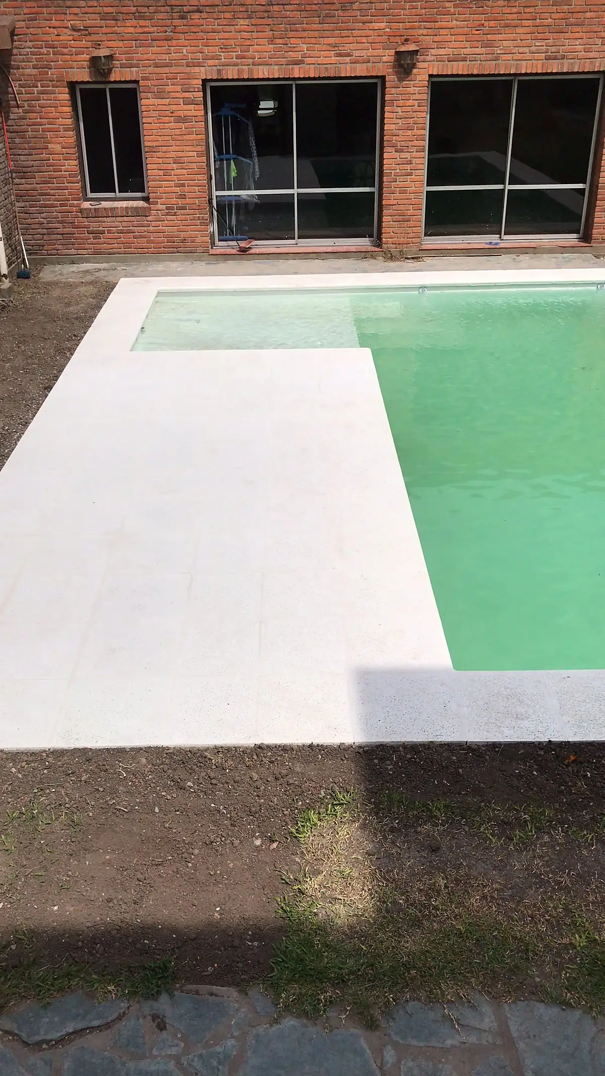 Piscina rectangular con solárium atérmico blanco en L frente a la galería de la casa