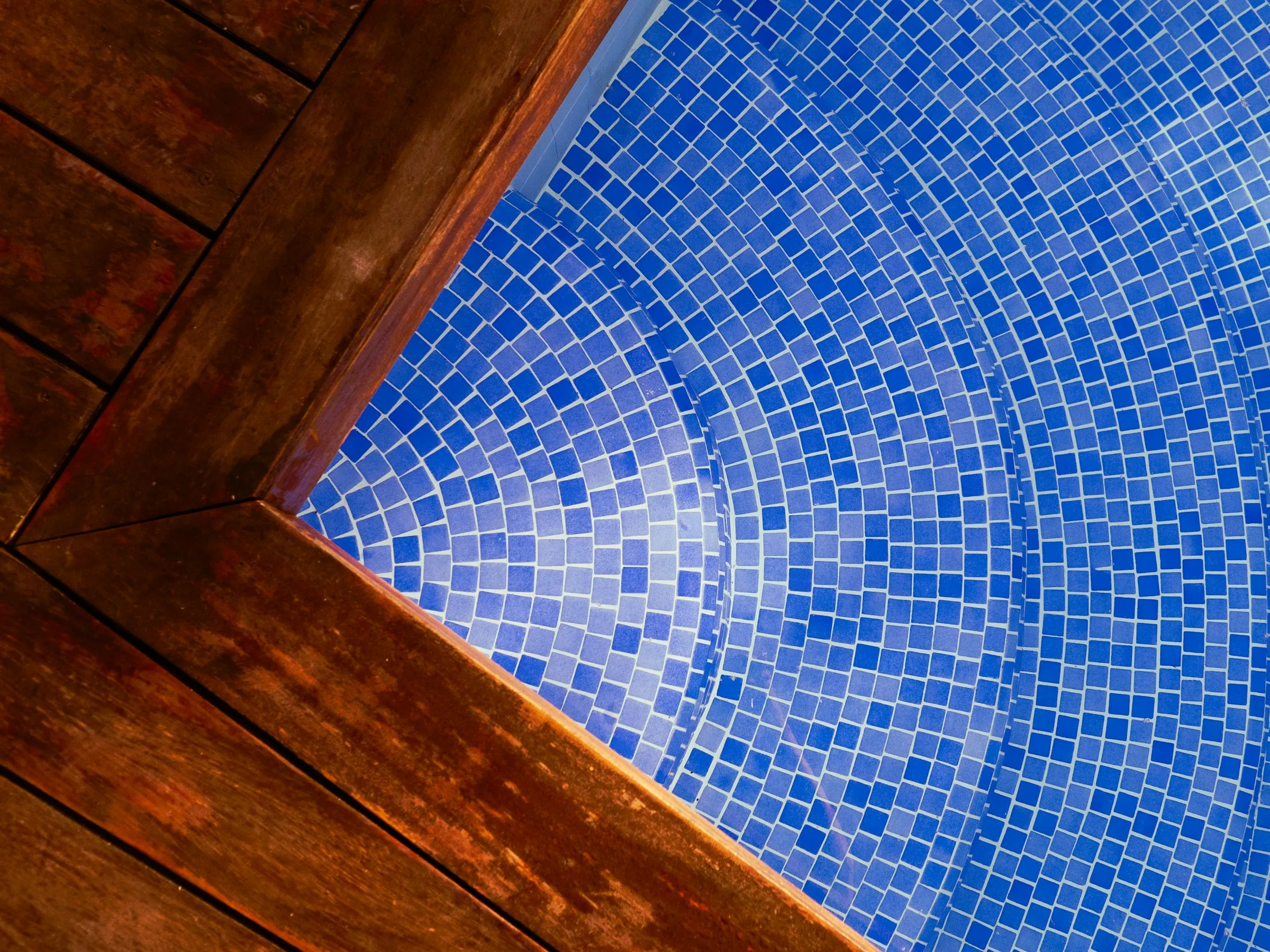 Piscina renovada con revestimiento veneciano azul y deck de madera